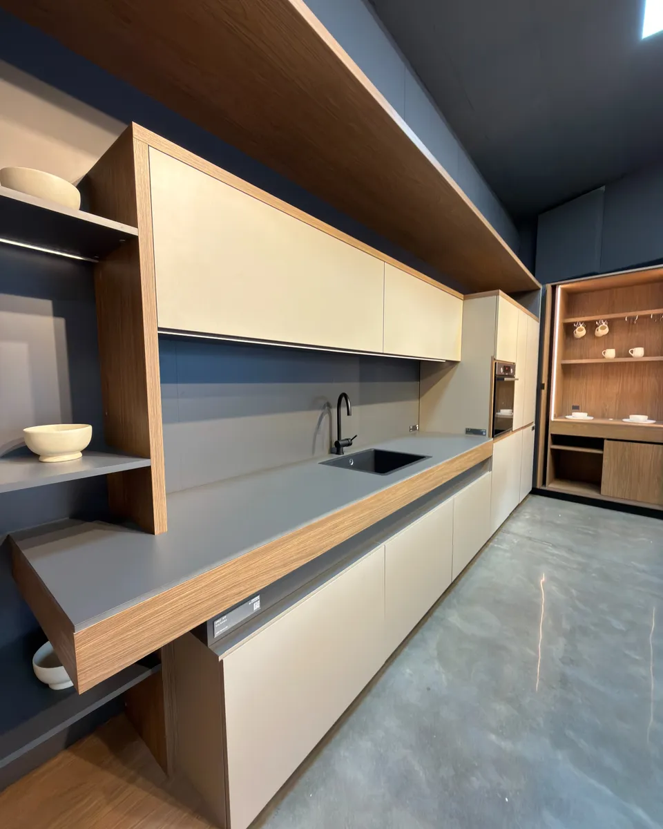 Mueble de cocina lineal en el showroom, con alacenas, mesada y estantes en dos tonos.